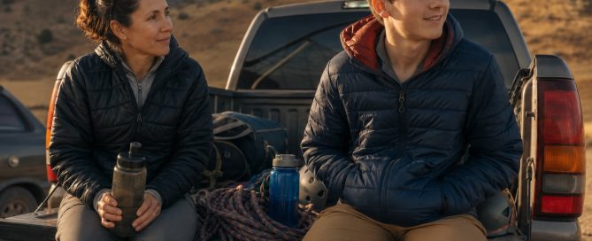 A life coach and a teenage boy sit on a pickup tailgate with climbing gear, talking in the foothills